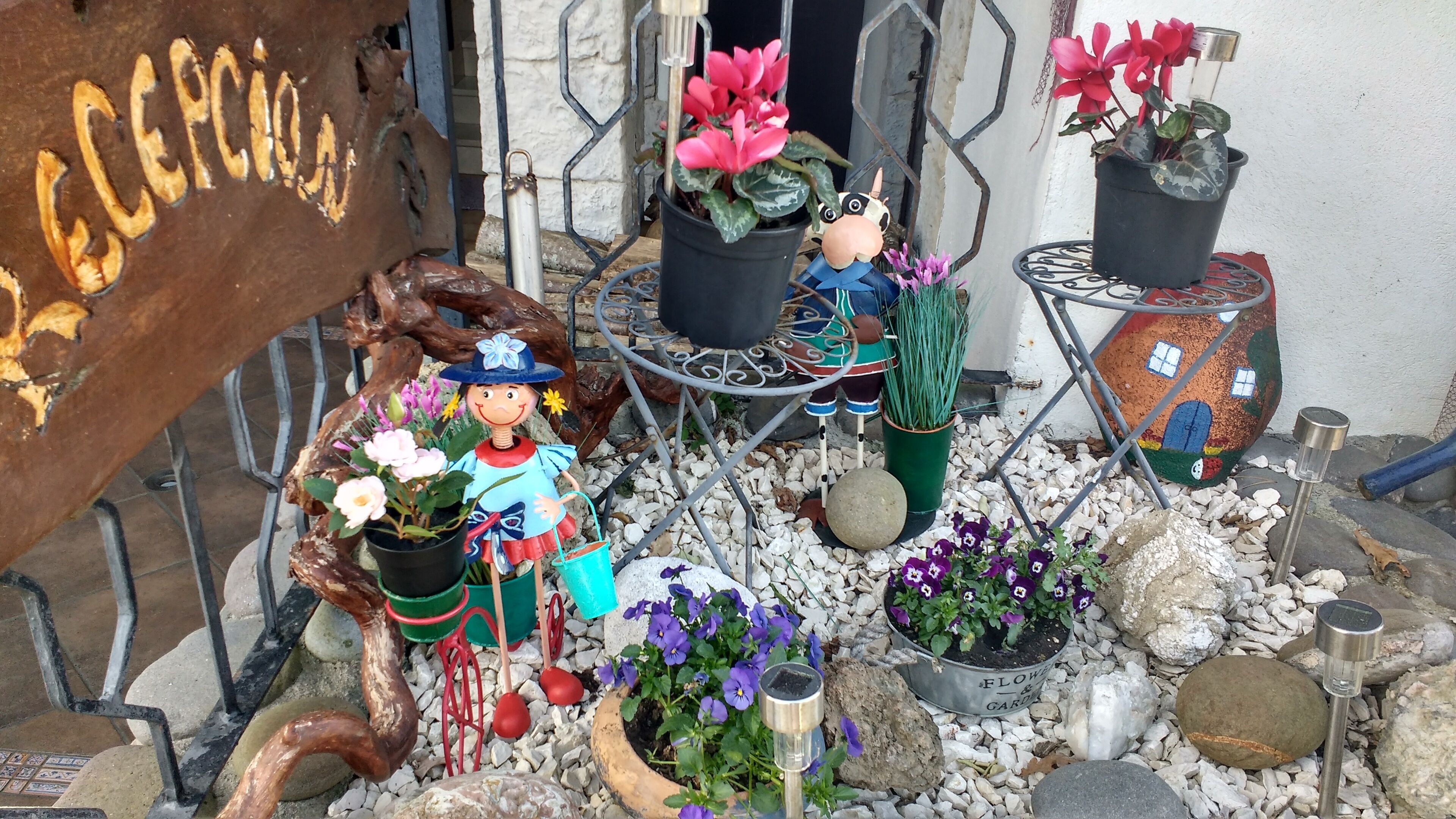 A garden with various potted plants, a metal sculpture, and a decorative sign.