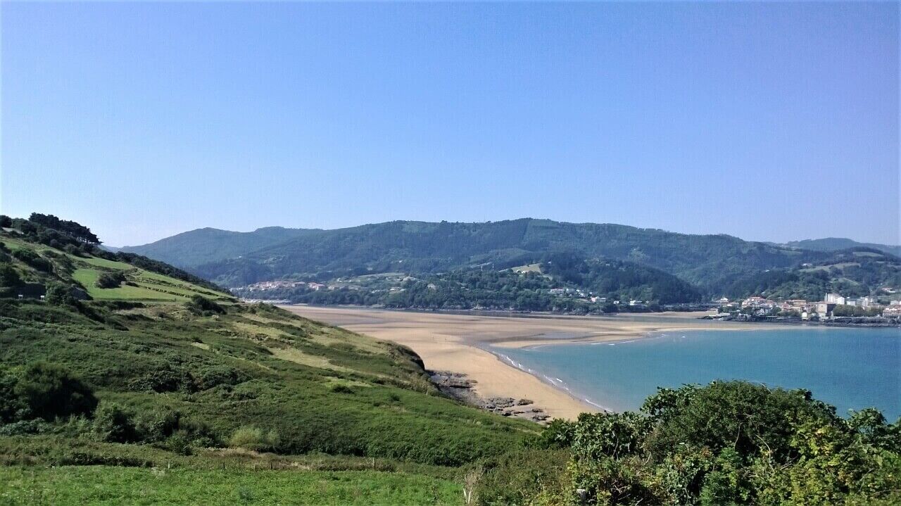 A coastal landscape with a beach, hills, and a town in the background.