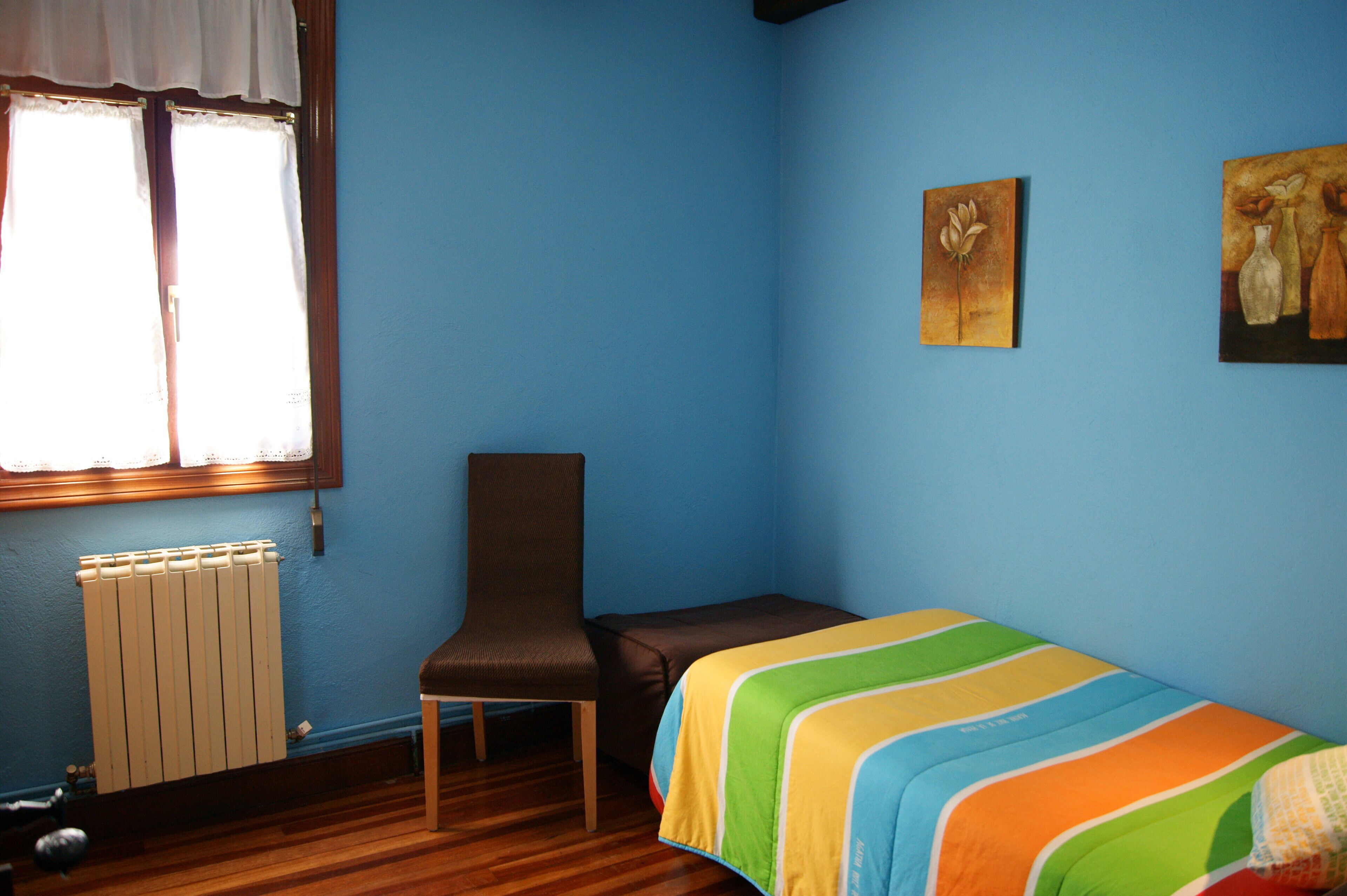 A room with a bed, a chair, a radiator, and two paintings on the wall.