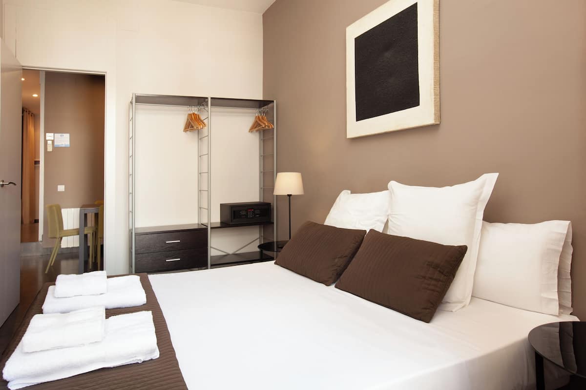 A hotel room with a bed, a desk, a chair, a wardrobe, and a framed picture on the wall.