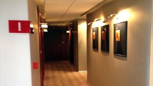 A hallway with patterned carpet, wall-mounted lights, and framed pictures. - Hotel Mone (Plovdiv)