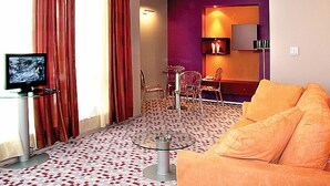 A modern living room with a glass coffee table, orange sofa, and a television on a stand. - Hotel Mone (Plovdiv)