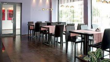 A modern dining area with tables and chairs, large windows, and a potted plant.