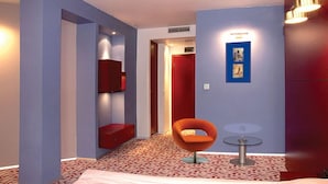A hotel room with a modern design, featuring a red accent wall, a unique orange chair, and a small table. - Hotel Mone (Plovdiv)