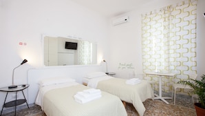 A hotel room with two beds, a small table, a chair, a potted plant, and a mirror on the wall. - Martini Bed (Rome)