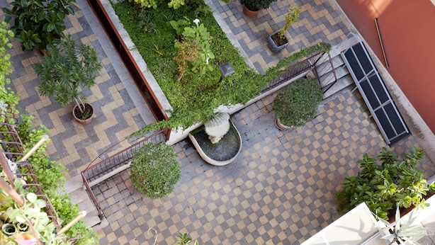 An aerial view of a courtyard with a checkered tile floor, potted plants, a small fountain, and a metal railing. - Martini Bed (Rome)