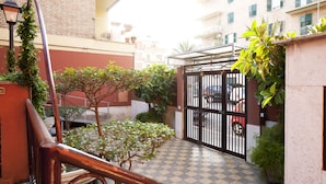 A courtyard with a checkered floor, potted plants, a metal gate, and a red car parked inside. - Martini Bed (Rome)
