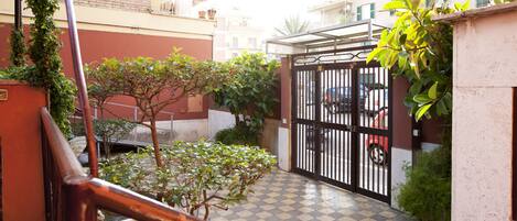 A courtyard with a checkered floor, potted plants, a metal gate, and a red car parked inside.