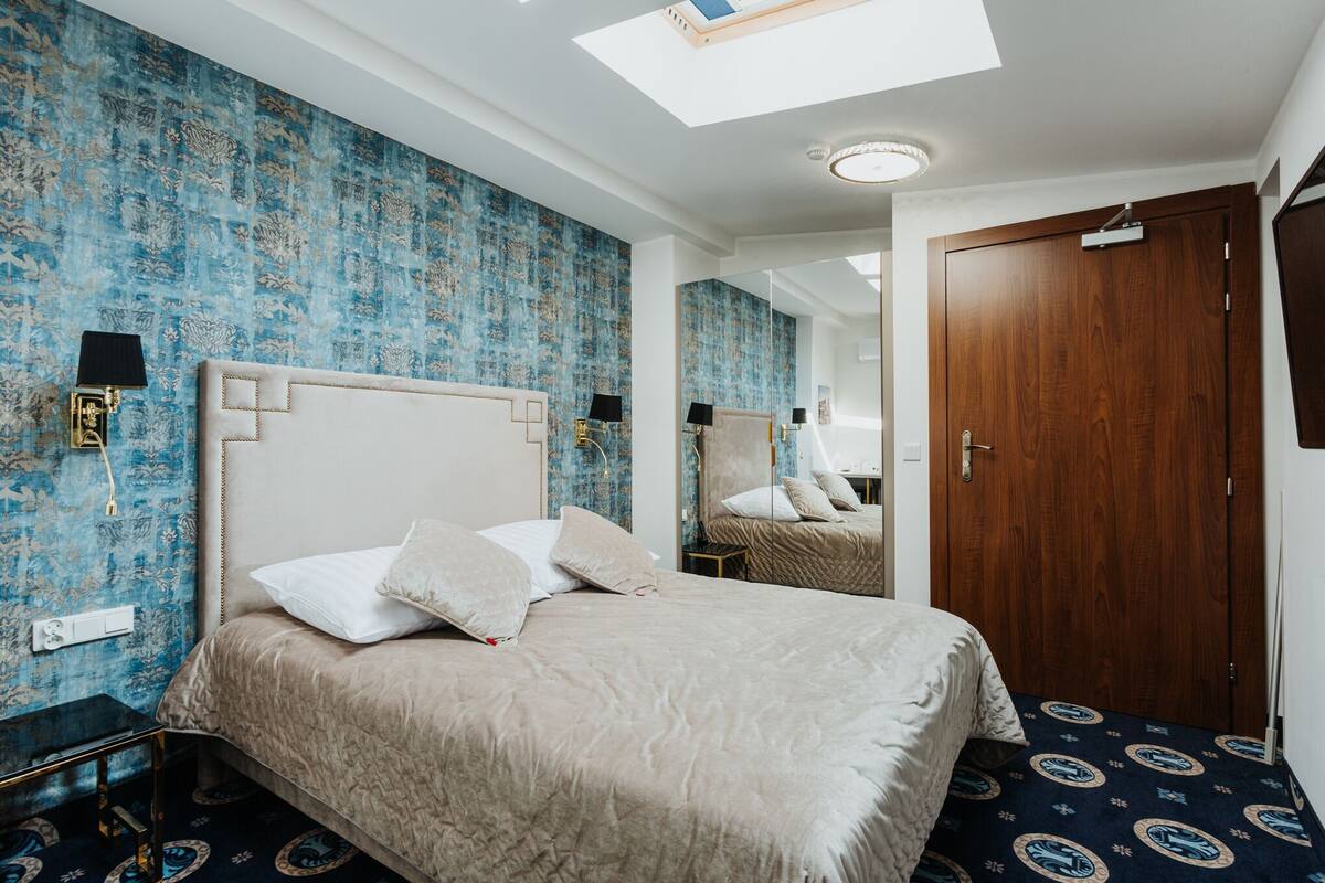 A hotel room with a large bed, a wooden wardrobe, a mirror, and a skylight.
