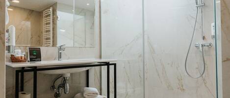 A modern bathroom with a glass-enclosed shower, a marble-tiled floor, a black metal shelf with towels, and a skylight.