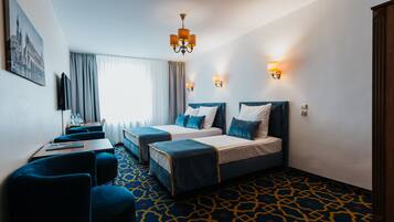 A hotel room with two beds, a desk, and a chair. There are two wall-mounted lamps and a chandelier.