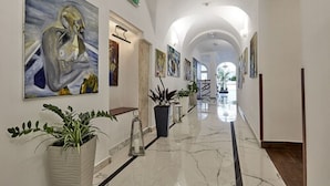 A hallway with a marble floor, framed artwork on the walls, and potted plants. - Hotel Jan (Kraków)