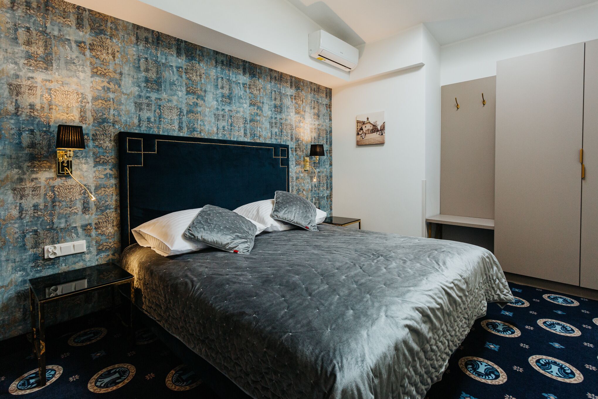 Une chambre à coucher avec un grand lit, une tête de lit à motifs géométriques, deux lampes de chevet, un climatiseur mural et une armoire avec un miroir.