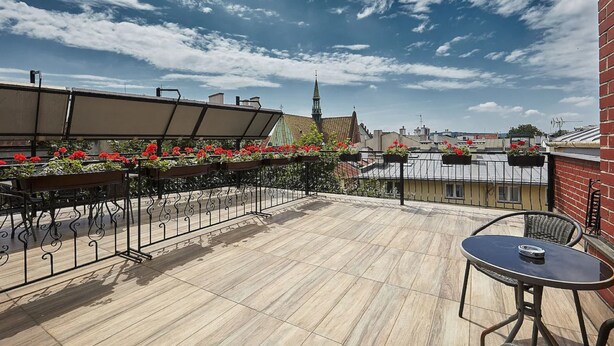 A rooftop terrace with a table and chairs, a view of a church spire, and red flowers in planters. - Hotel Jan (Kraków)