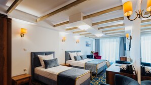 A hotel room with two beds, a desk, a chair, and a window with curtains. - Hotel Jan (Kraków)