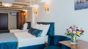 A hotel room with two beds, a blue chair, a wooden table, and a vase of flowers.