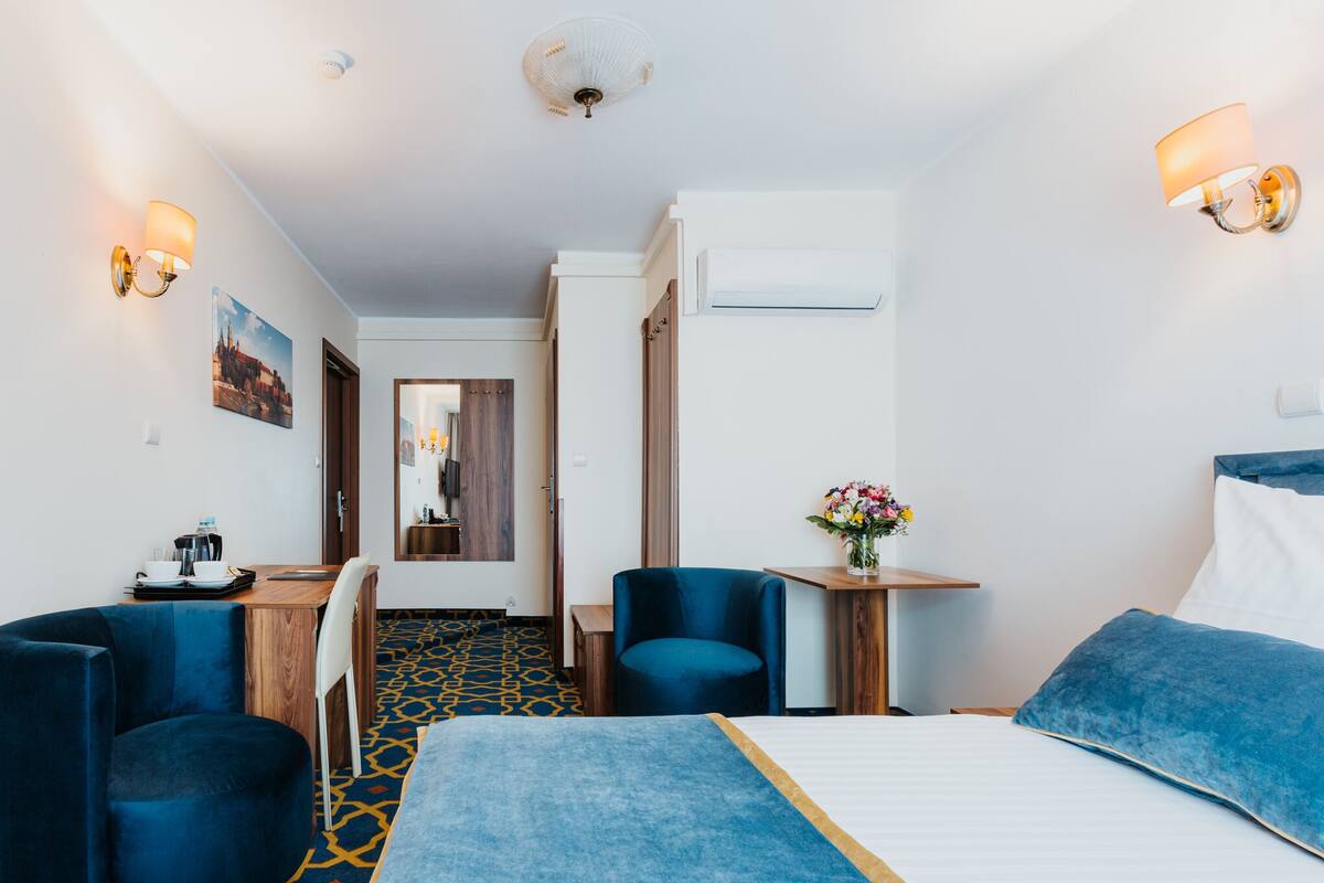 A hotel room with a bed, two chairs, a desk, and a small table with a vase of flowers.