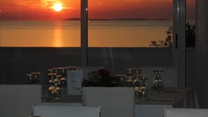 Une table dressée pour le dîner, avec vue sur un coucher de soleil sur l’eau.