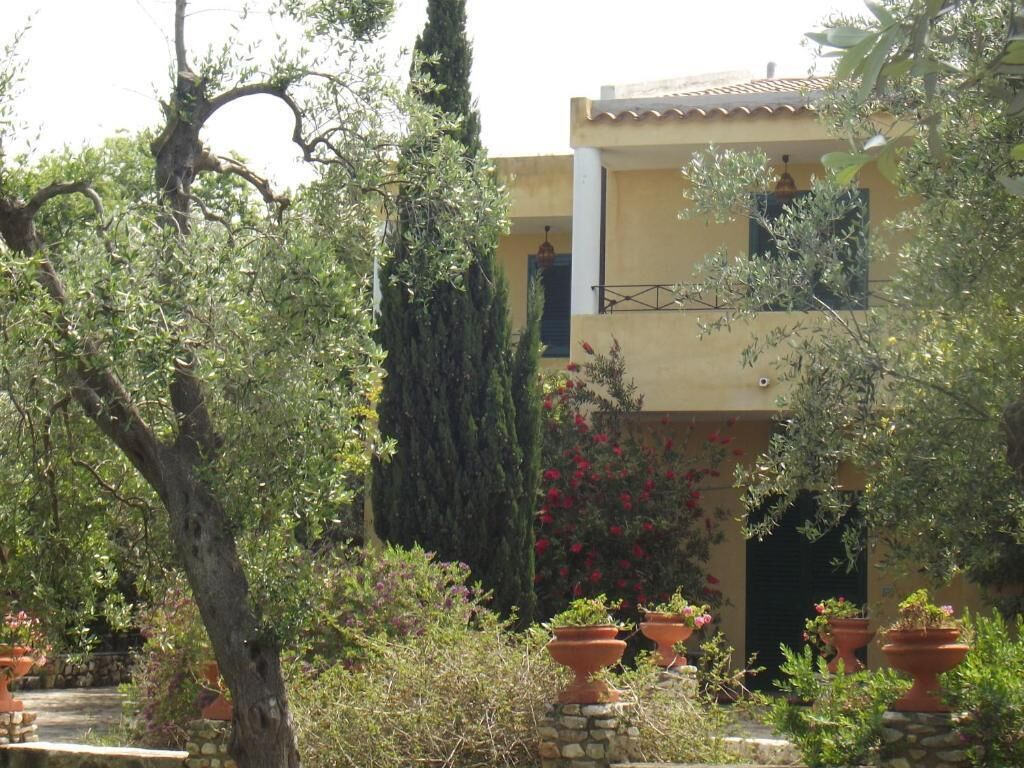 A building with a balcony, surrounded by trees and potted plants.