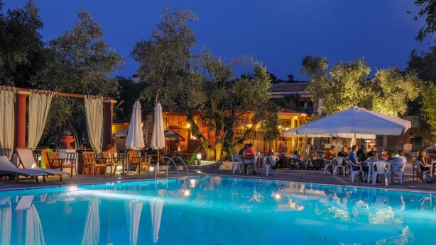 Une piscine entourée d’arbres et d’immeubles, avec des chaises longues et des parasols.