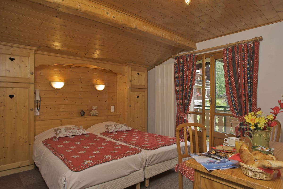 Ein Zimmer in einer Holzhütte mit zwei Betten, einem Esstisch mit Frühstück und einem Fenster mit Vorhängen.