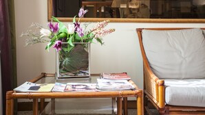 Een kamer met een glazen vaas bloemen op een bijzettafeltje, een stoel met een kussen en een tijdschrift op de tafel.