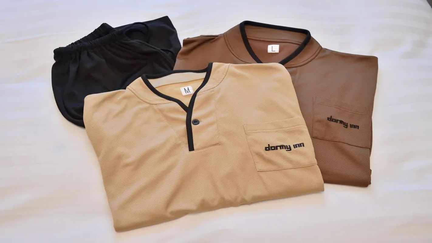 Three folded shirts with 'darmy inn' branding, laid out on a bed.