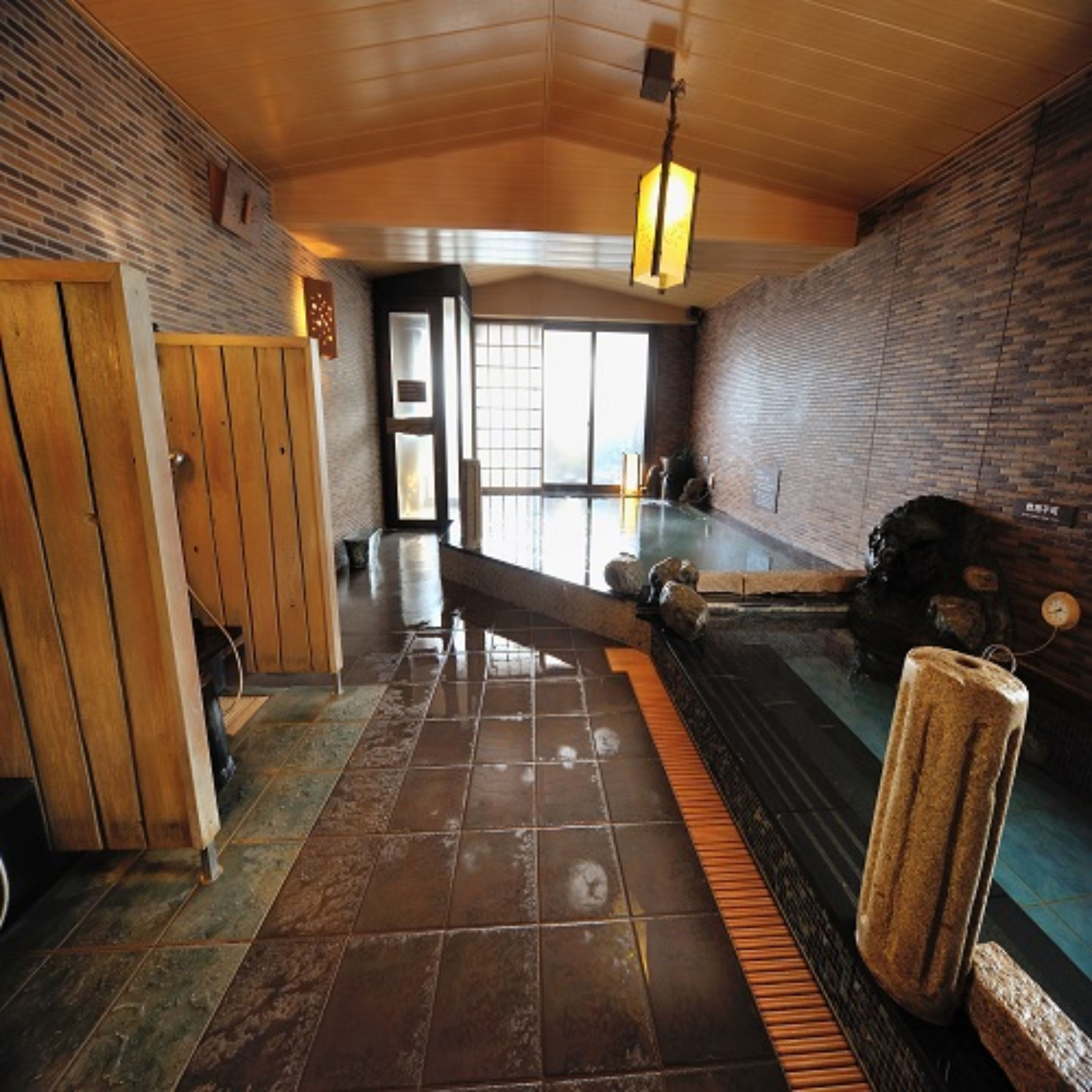Ein traditionelles japanisches Onsen mit Holzinnenraum, einem Steine-Thermalbad und Blick ins Freie.