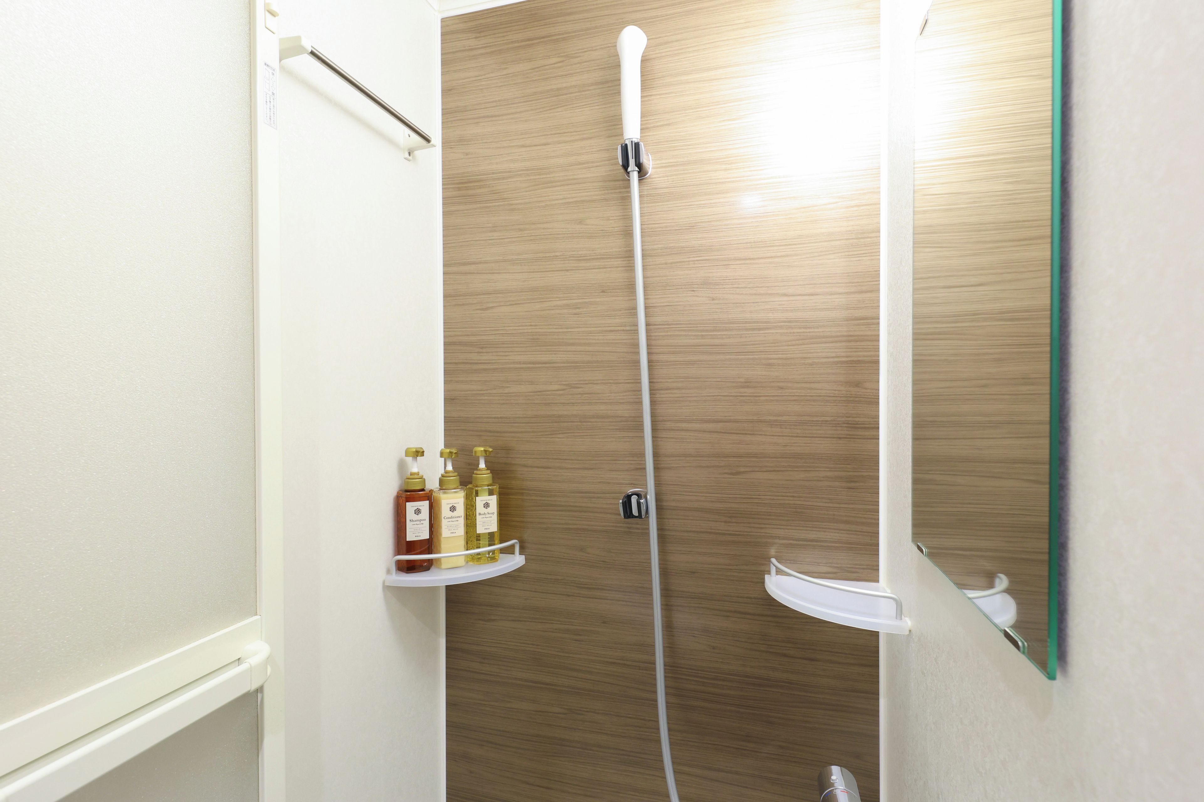 Un baño con puerta de madera, ducha blanca y repisas con artículos de aseo.