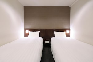 Una habitación de hotel con dos camas individuales, un cabecero oscuro y lámparas de noche.
