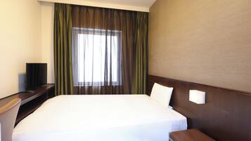 A hotel room with a large bed, a bedside table with a lamp, a TV, and a window with curtains.