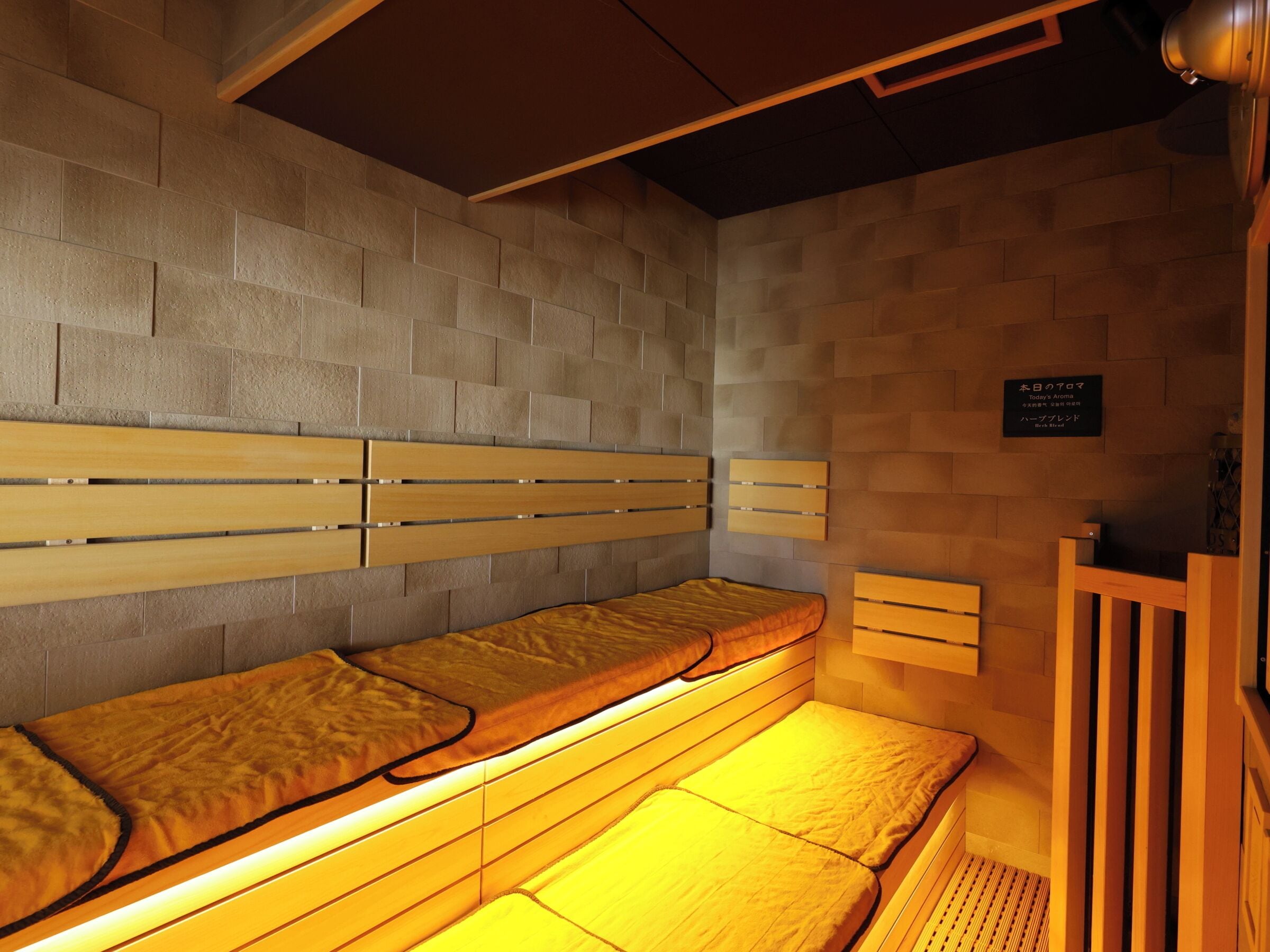 Un sauna con bancos de madera y bancos con cojines. Hay un cartel en la pared y una estructura de madera a la derecha.