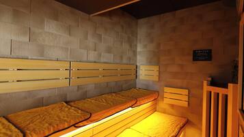 A sauna room with wooden benches and benches with cushions. There is a sign on the wall and a wooden structure on the right.
