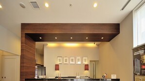 A reception area with a wooden counter, two wooden stools, framed pictures on the wall, and a poster on the right. - Dormy Inn Matsumoto Natural Hot Spring (Matsumoto)