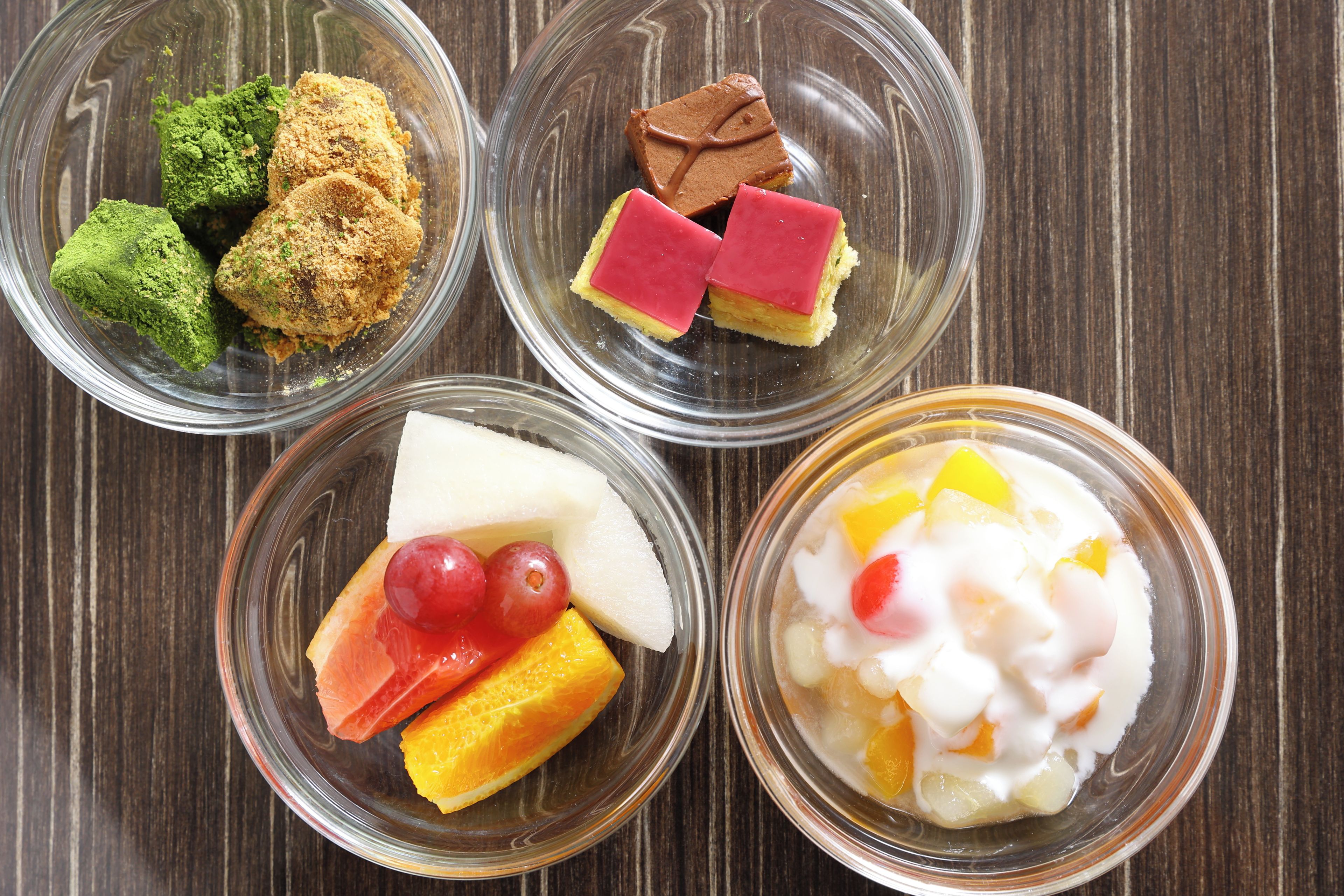 Four glass bowls containing different food items on a wooden surface.