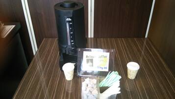 A coffee machine, a sign reading "Welcome Coffee", and two disposable cups on a table.