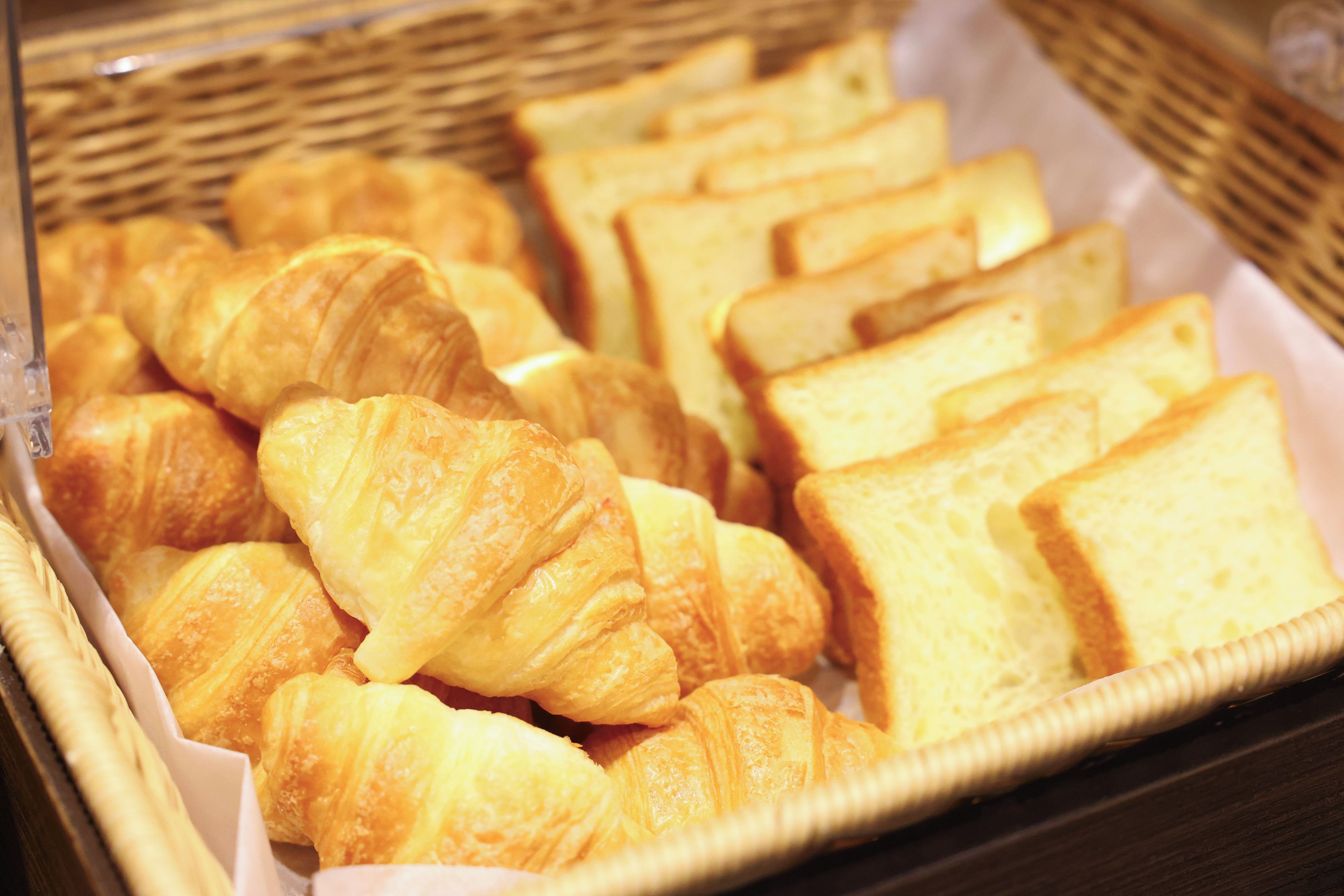 Una cesta con varios productos horneados, incluyendo croissants y rebanadas de pan.