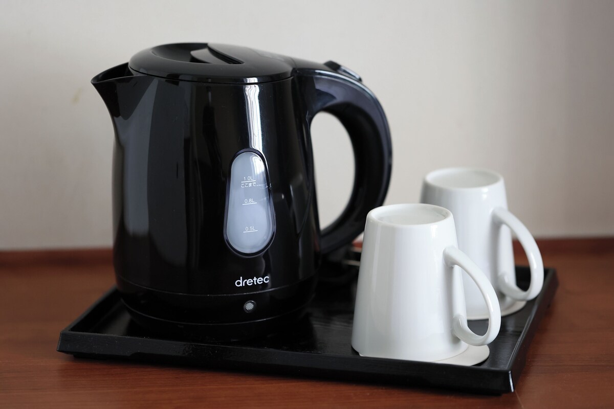 A black electric kettle with measurement markings and two white mugs on a black tray.