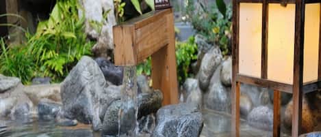 A wooden bench with a sign, a small water feature with rocks, and a traditional Japanese lantern.