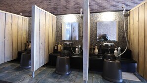 A public restroom with wooden partitions, a tiled floor, and a brick wall. - Dormy Inn Matsumoto Natural Hot Spring (Matsumoto)