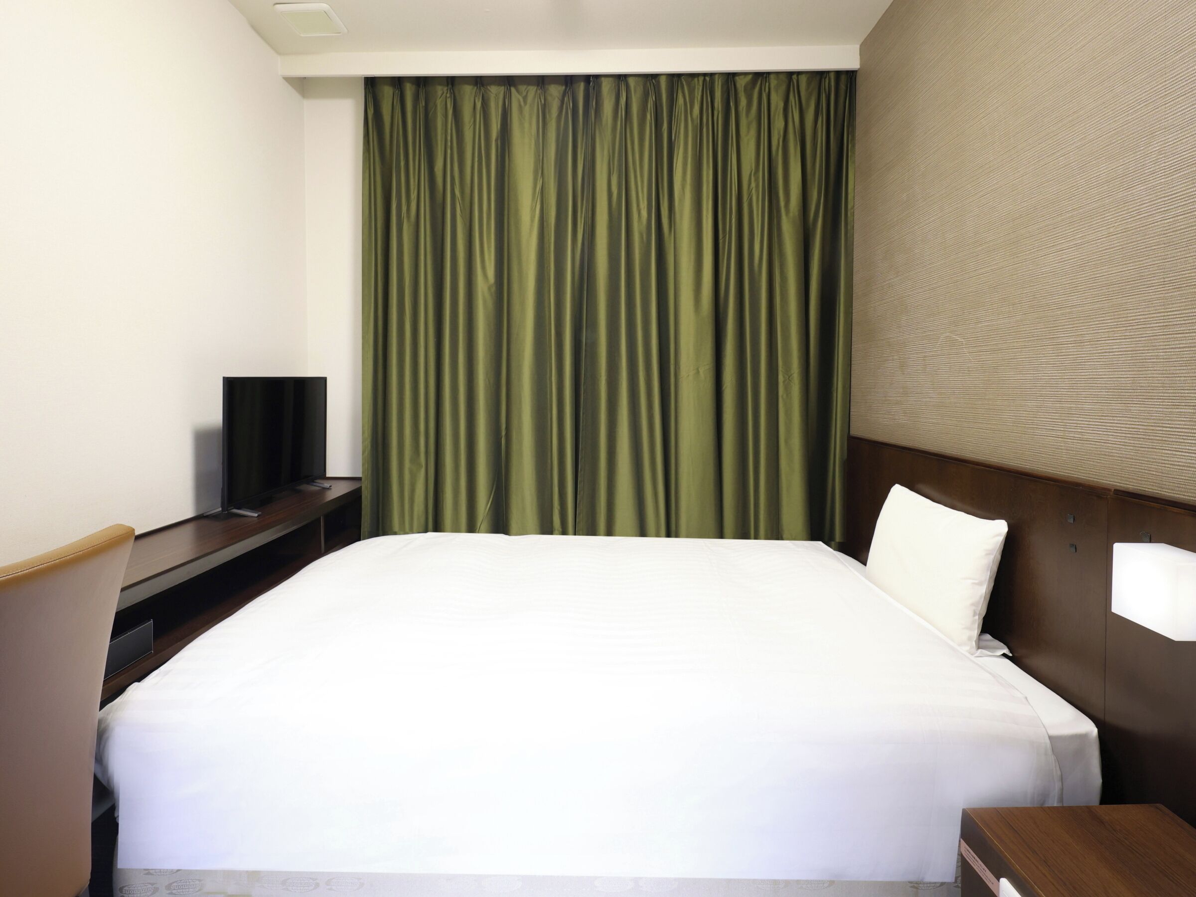 Une chambre d’hôtel avec un lit, un téléviseur posé sur un meuble, un bureau et un rideau vert.