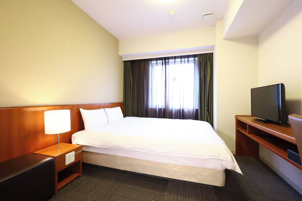 A hotel room with a large bed, a TV on a wooden stand, and a nightstand with a lamp.