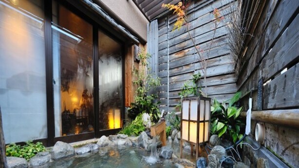 A stone-tiled hot spring area with a wooden fence, a lantern, and a wooden bench. - Dormy Inn Matsumoto Natural Hot Spring (Matsumoto)