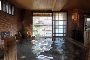 A traditional Japanese onsen with a wooden interior, a stone basin, and a view of the outside through a sliding door. - Dormy Inn Matsumoto Natural Hot Spring (Matsumoto)