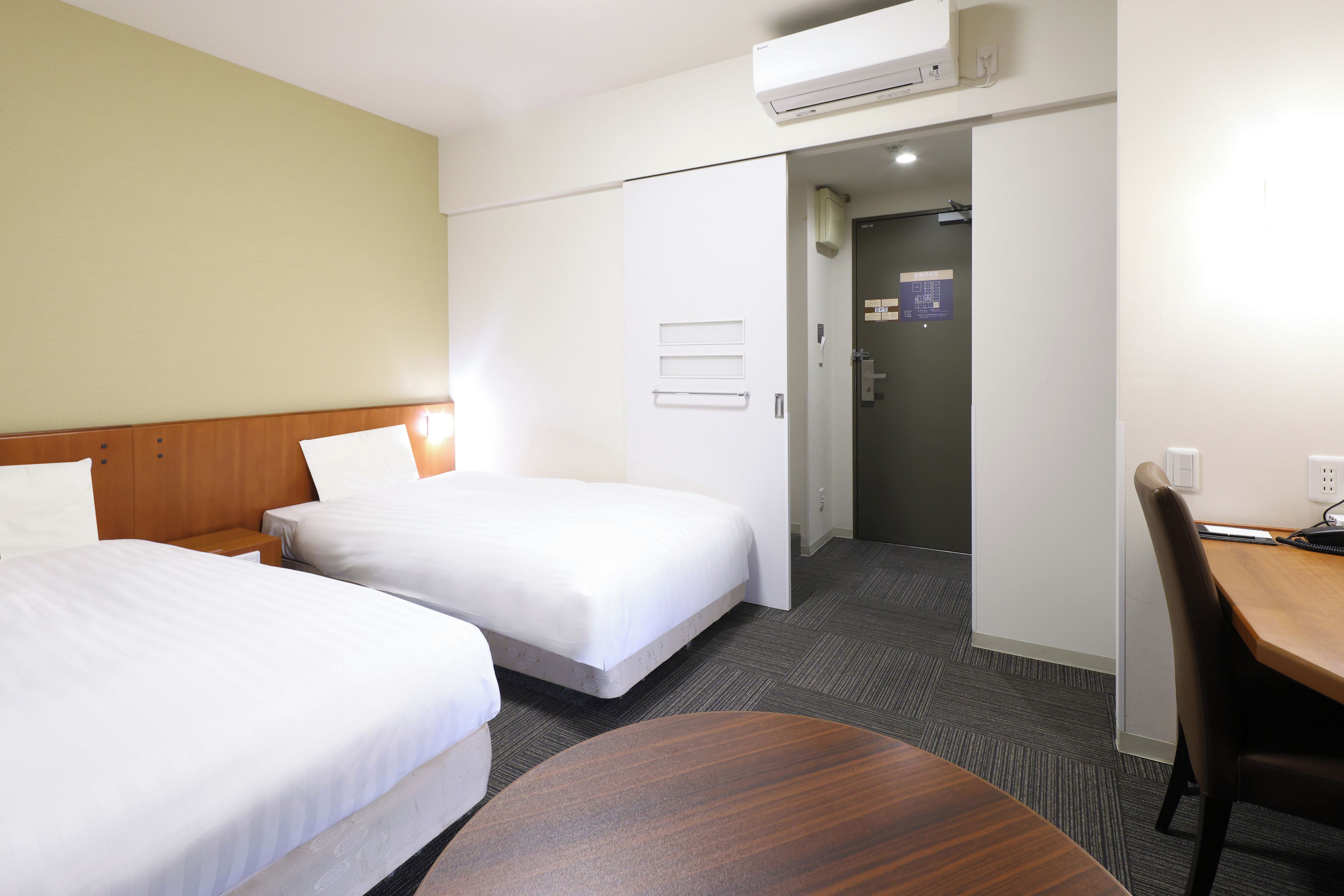 A hotel room with two beds, a desk, and a chair.