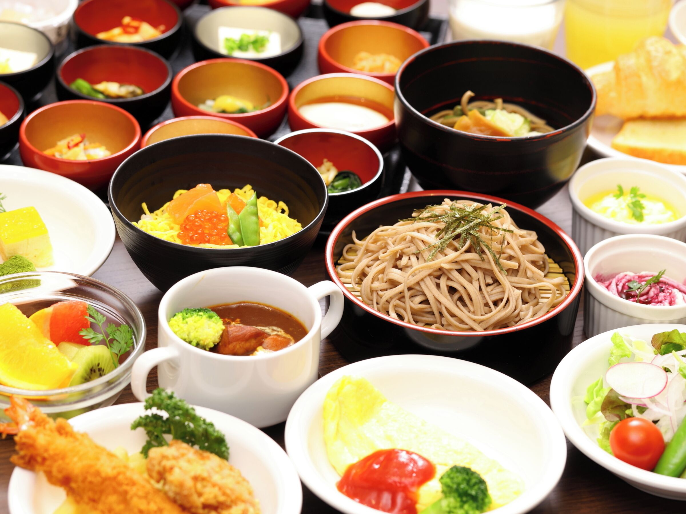 Variedad de platos que incluyen fideos, sushi y una ensalada, lo que sugiere una amplia selección de comidas.