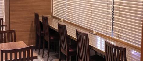A dining area with wooden tables and chairs, a tiled floor, and a window with blinds.