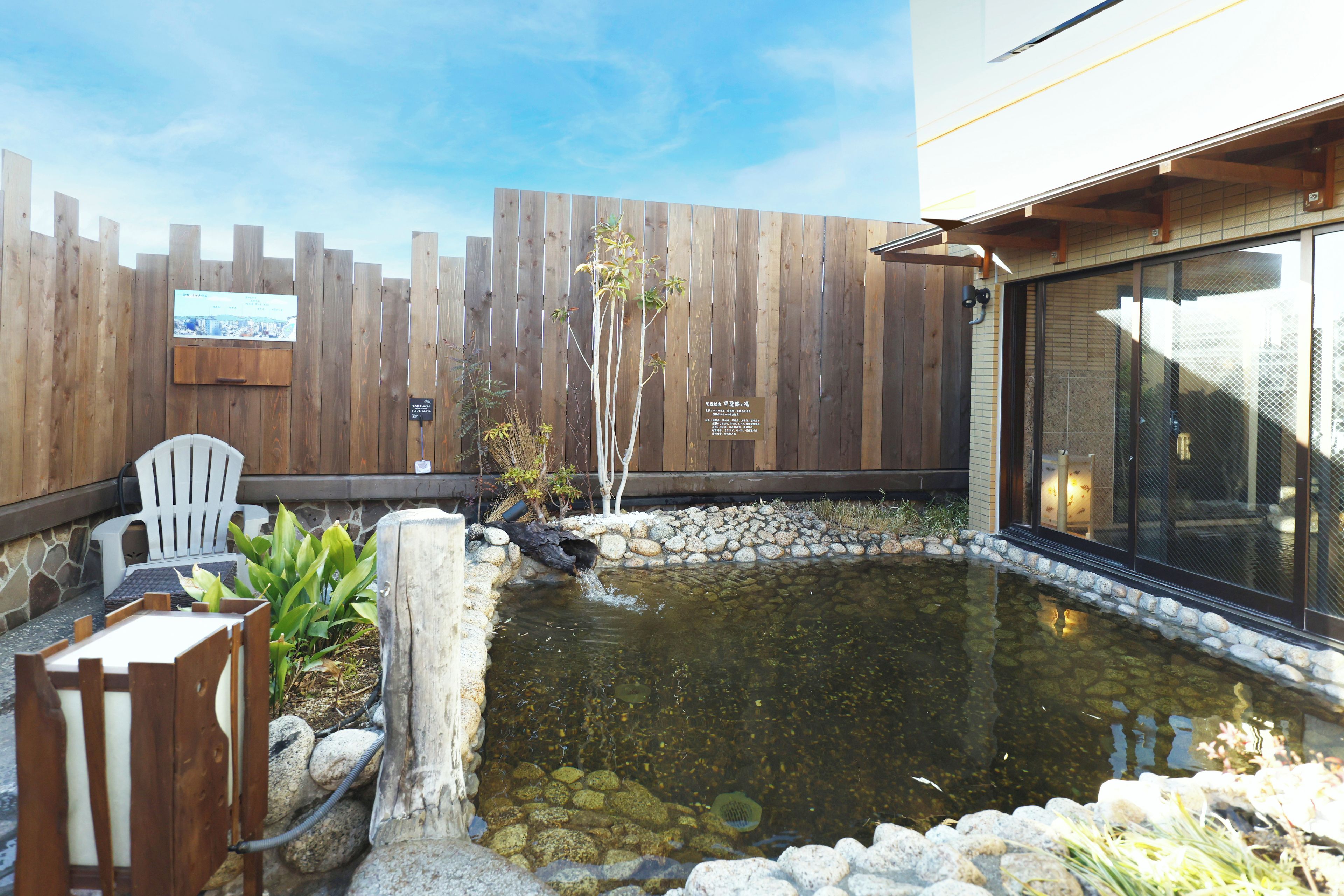 A backyard with a wooden fence, a small pond, and a seating area with a table and chairs.
