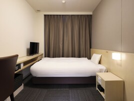 Habitación de hotel con cama, escritorio con televisor, mesita de noche y lámpara de pared.