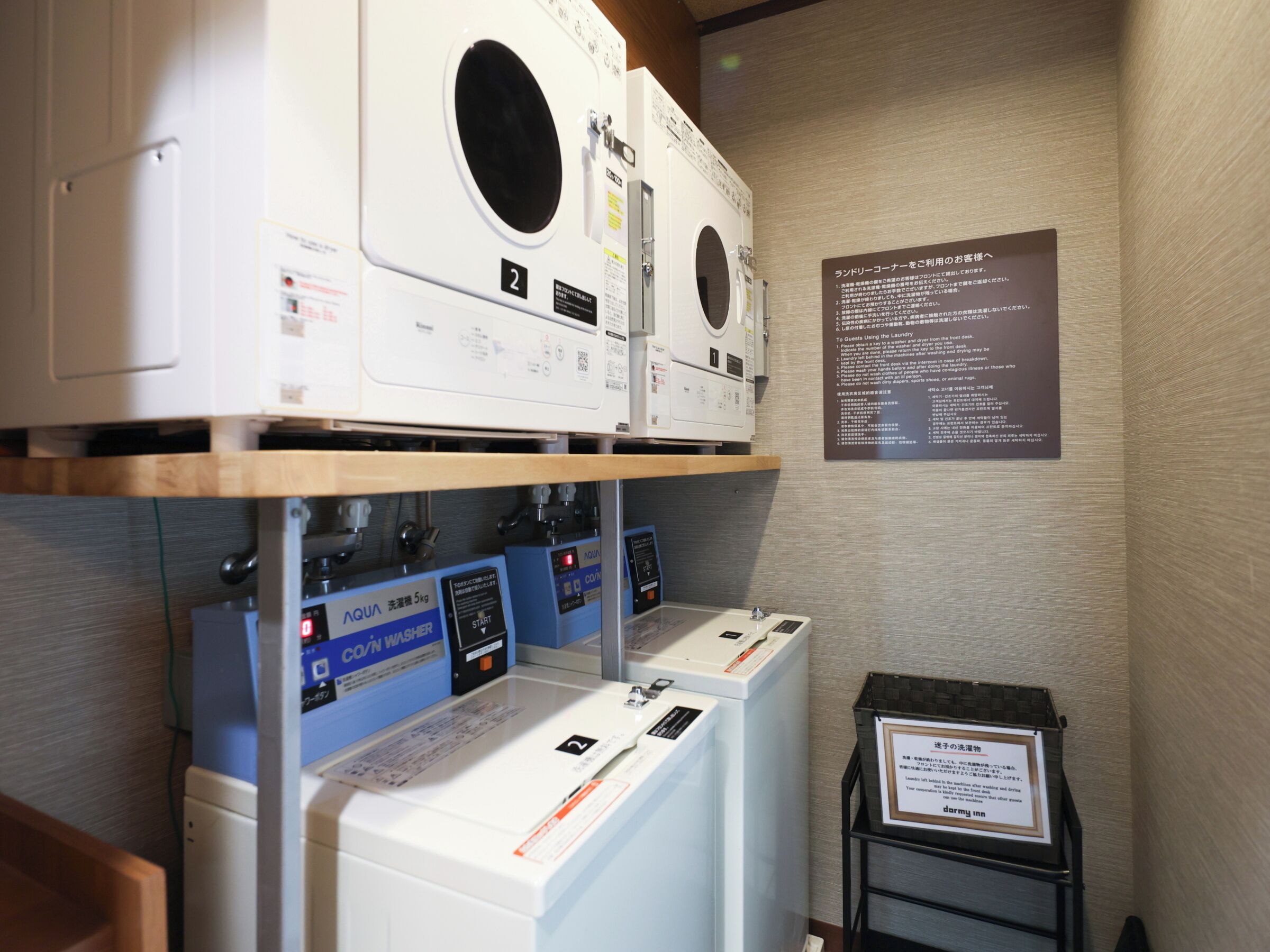 A laundry facility with multiple washing machines and dryers, a control panel, and informational signs.